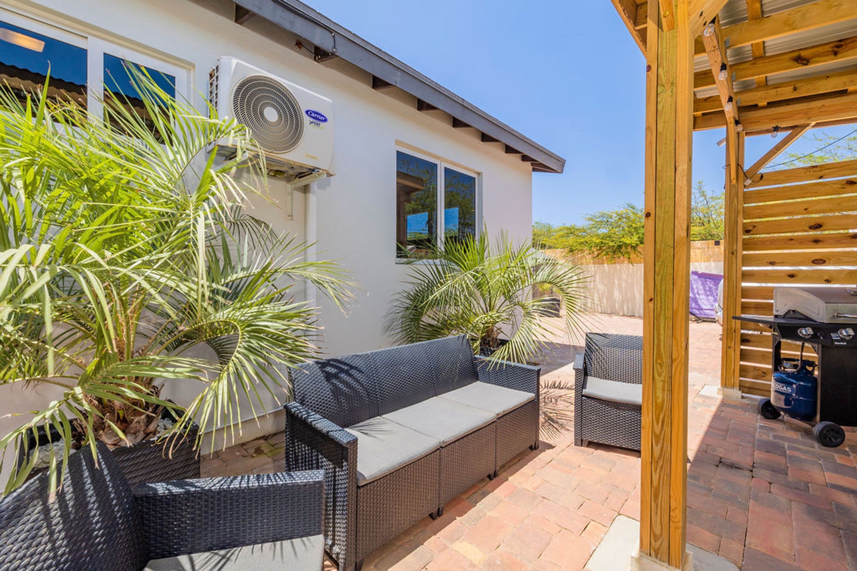 Eine Terrassenfläche mit Korbmöbeln, einem Grill und Kübelpflanzen.