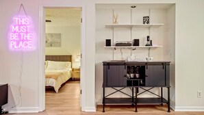 A modern room with a bed, a desk with shelves, and a neon sign.
