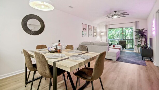 A dining area with a wooden table, cushioned chairs, and a hanging light fixture.