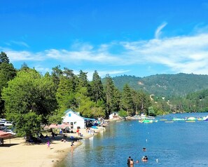 A lakeside beach with people swimming and sunbathing, surrounded by dense forest and hills. - Lake House Getaway - 2 bedroom home in peaceful Crestline with WiFi AC and more! (Crestline)