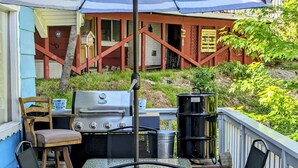 An outdoor patio with a grill, chairs, and a table under a striped umbrella.