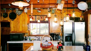 A kitchen with wooden cabinets, a stainless steel refrigerator, hanging light fixtures, and a window with a view.