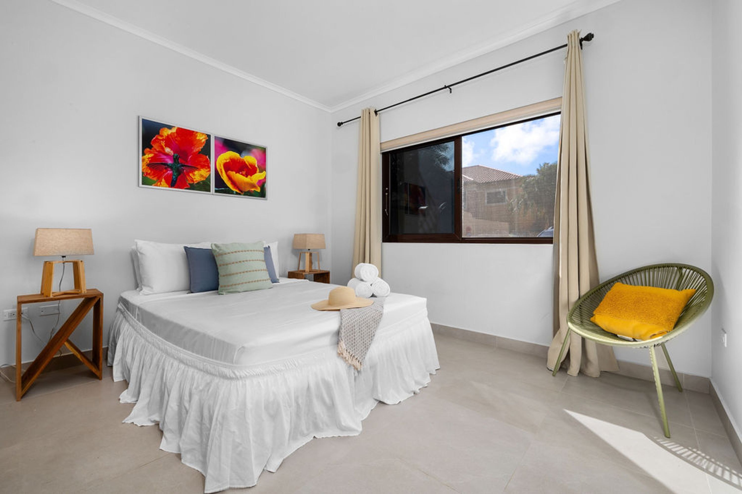 A bedroom with a bed, two bedside tables, a window with curtains, and a chair.