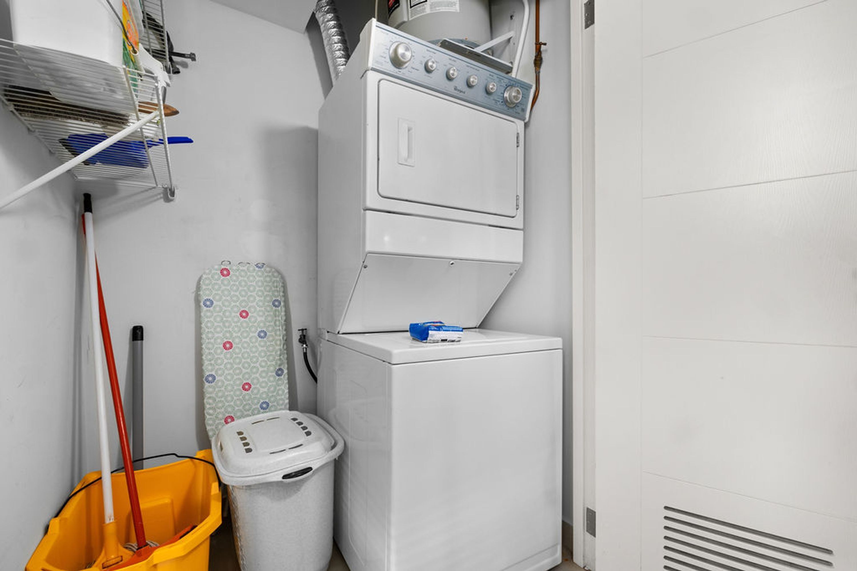 Un espace dédié à la lessive, comprenant un lave-linge, une planche à repasser, une serpillière et une poubelle.