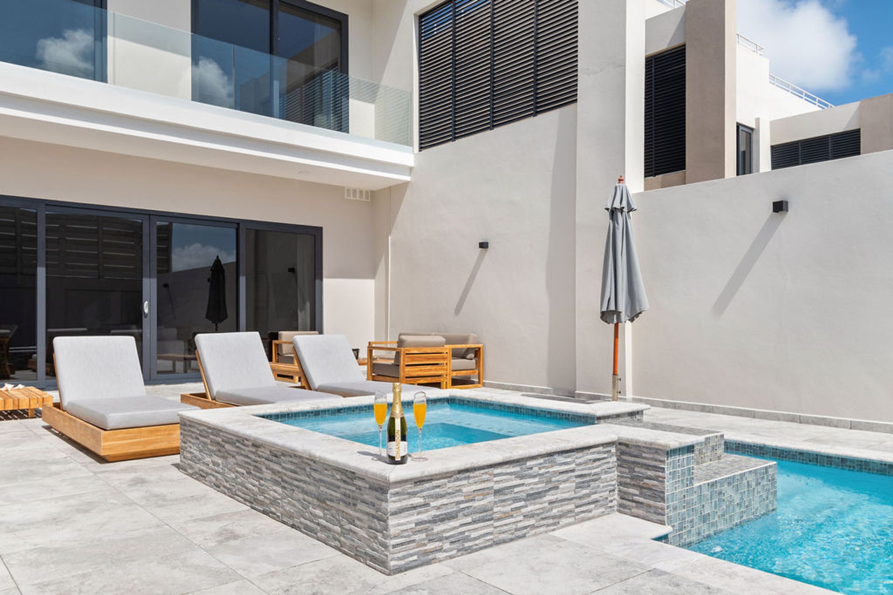 Un área de piscina exterior moderna con escalones de piedra, sillones de descanso y una mesa con sombrillas.
