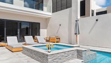 Un área de piscina exterior moderna con escalones de piedra, sillones de descanso y una mesa con sombrillas.