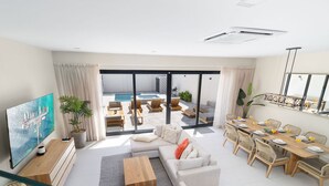 Una sala de estar moderna con televisor de pantalla plana, asientos cómodos, un comedor y vistas a una piscina exterior.