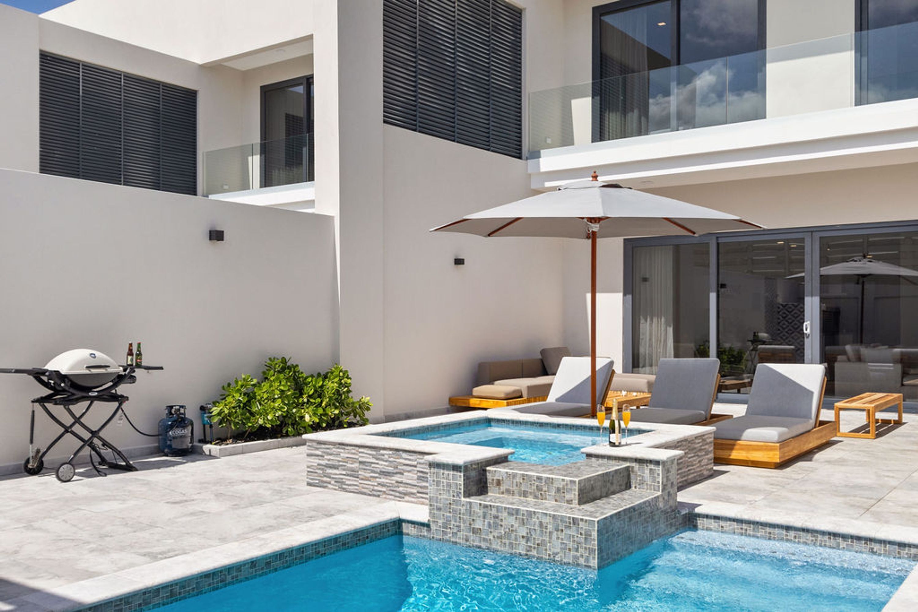 A modern outdoor pool area with a hot tub, lounge chairs, and a barbecue grill.
