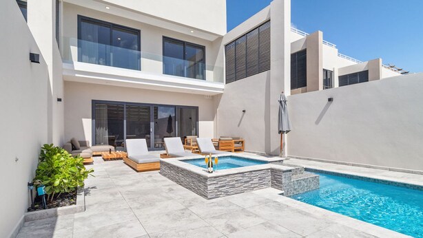 Una casa moderna de dos pisos con piscina, mobiliario exterior y un amplio acceso por puerta de vidrio.
