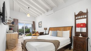 A spacious bedroom with a large bed, wooden headboard, and a wooden nightstand with a lamp. - Tropical Getaway Near Arikok National Park Pool (Santa Cruz)