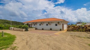 A single-story house with a red-tiled roof, a stone wall, and a paved driveway. - Tropical Getaway Near Arikok National Park Pool (Santa Cruz)