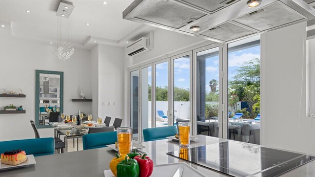 Cozinha moderna com uma ilha grande, área de jantar com cadeiras azuis e vista para o exterior.