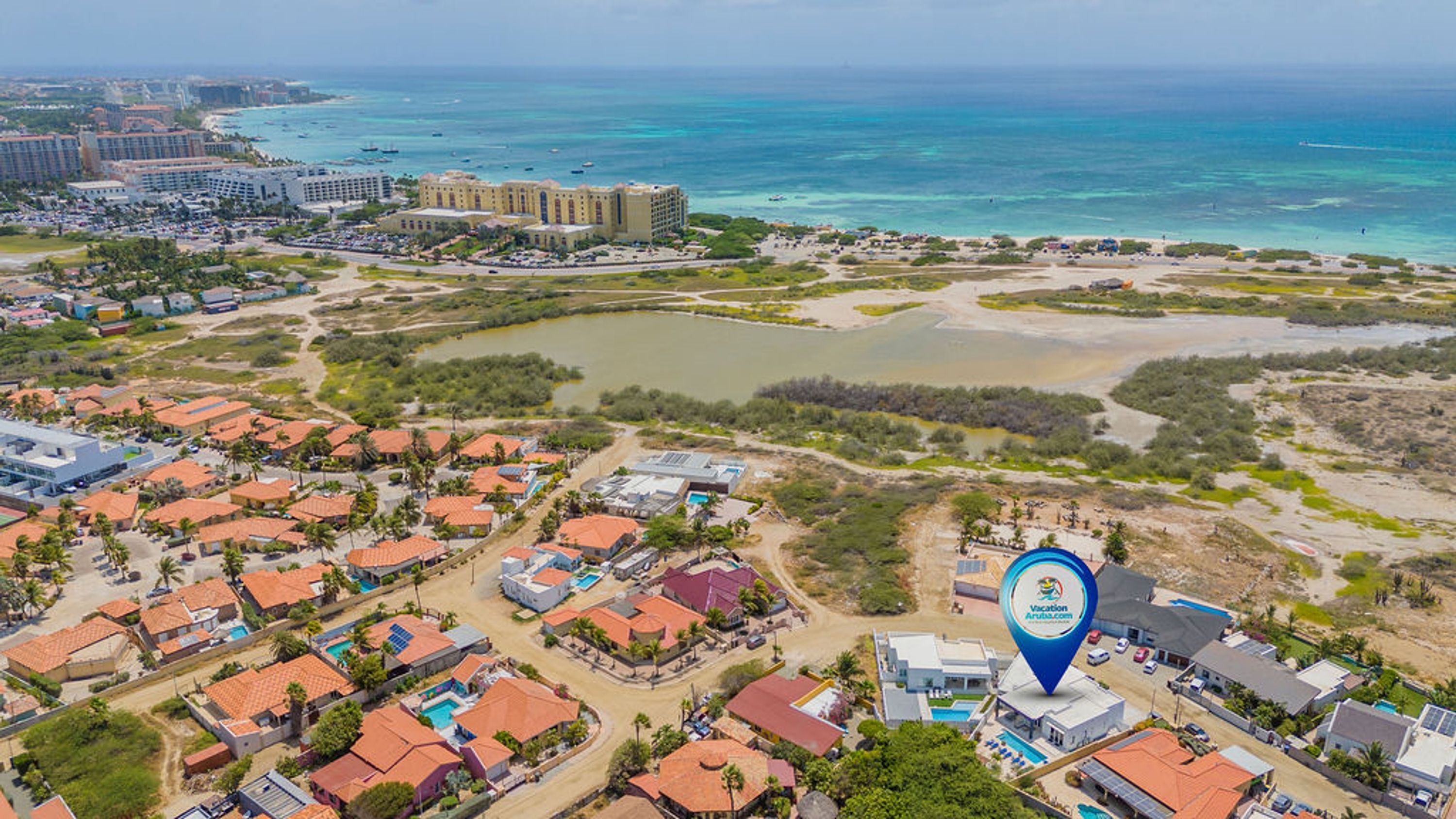 Luchtbeeld van een kustresort met meerdere gebouwen, waaronder hotels en woonhuizen, omgeven door stranden en helderblauw water.