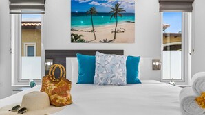 Quarto de hotel com uma cama, um quadro com tema praiano e vista para a praia pela janela.
