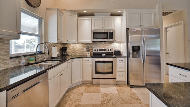 Una cocina con armarios blancos, electrodomésticos de acero inoxidable, microondas, horno y refrigerador.