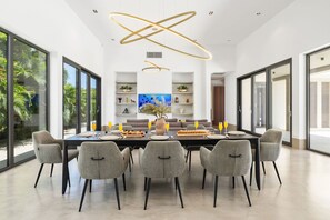 Un espace de salle à manger moderne, doté d’une grande table, de chaises grises et d’un luminaire au plafond au design original.