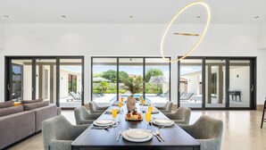 Ein Essbereich mit einem für sechs Personen gedeckten Tisch, einer Couch und Blick auf einen Pool und Sitzgelegenheiten im Freien.