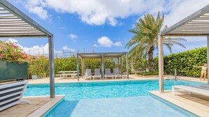 A swimming pool with lounge chairs and a pergola structure. - Serene Designer Gem Walk to Beach Strip Pool (Noord)