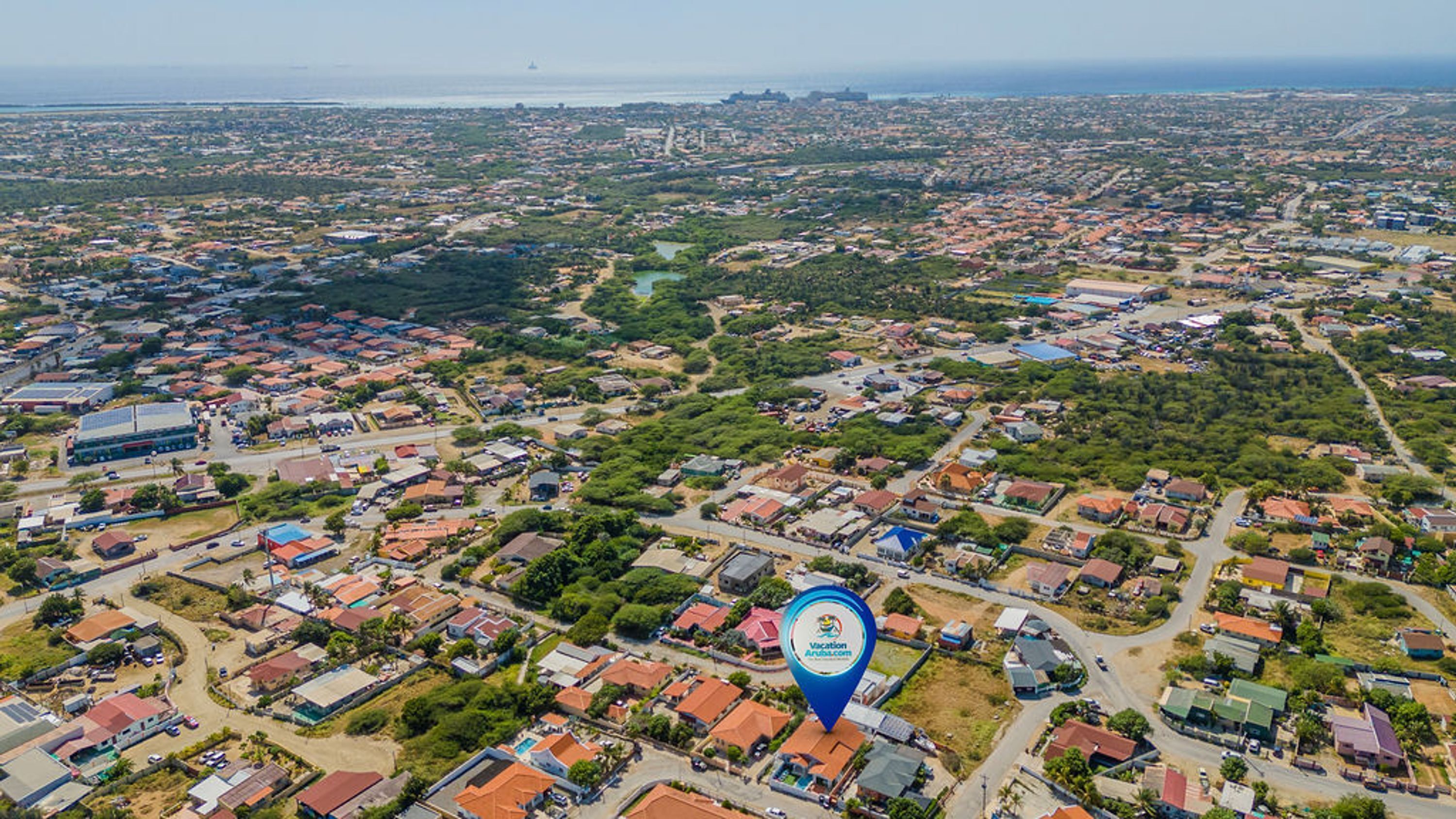 An aerial view of a residential area with houses, roads, and a large body of water in the background.