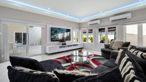 A modern living room with a flat-screen TV, a glass coffee table, and a sofa with patterned cushions.