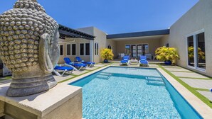 A swimming pool with blue lounge chairs, a decorative stone sculpture, and a modern building with large windows.