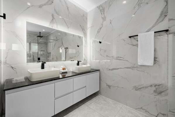 Une salle de bain moderne avec des murs en marbre, un grand miroir, deux lavabos et un porte-serviettes.