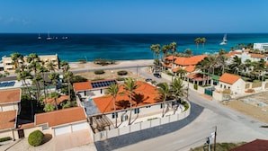 Una zona residenziale costiera con case dai tetti in tegole rosse, palme e vista sull'oceano con vele.