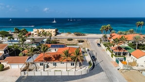 Una zona costiera con una strada che conduce a una spiaggia, circondata da edifici con tetti rossi e palme.