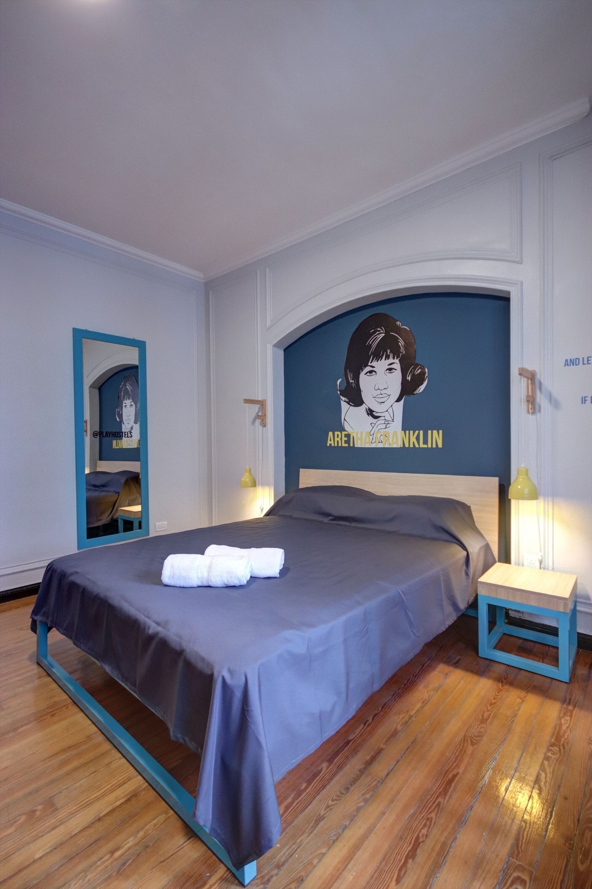 Una cama bien hecha con cabecera azul, un espejo y una pared con un cartel.