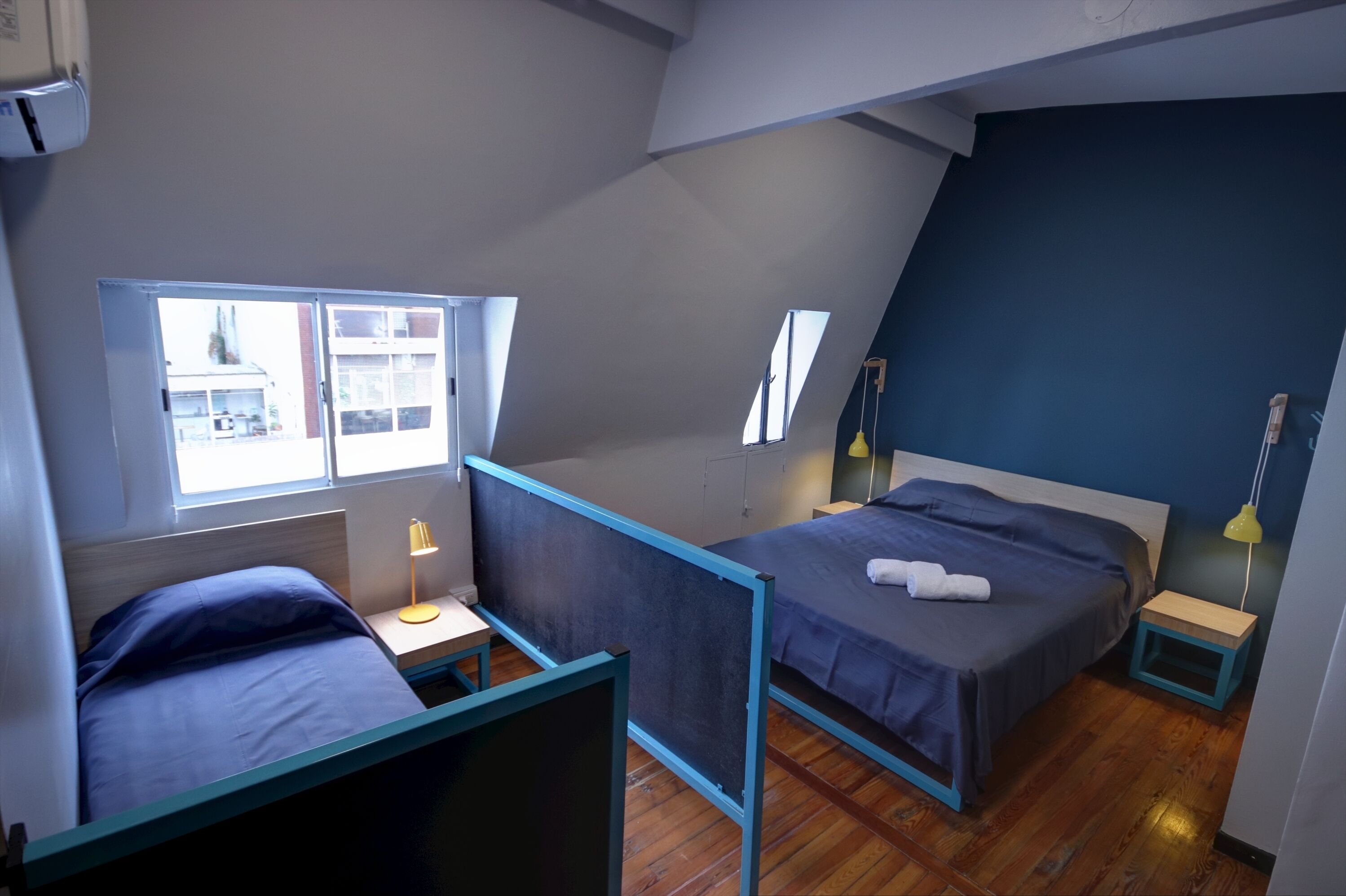 A bedroom with two beds, a window, and a small table with a lamp.