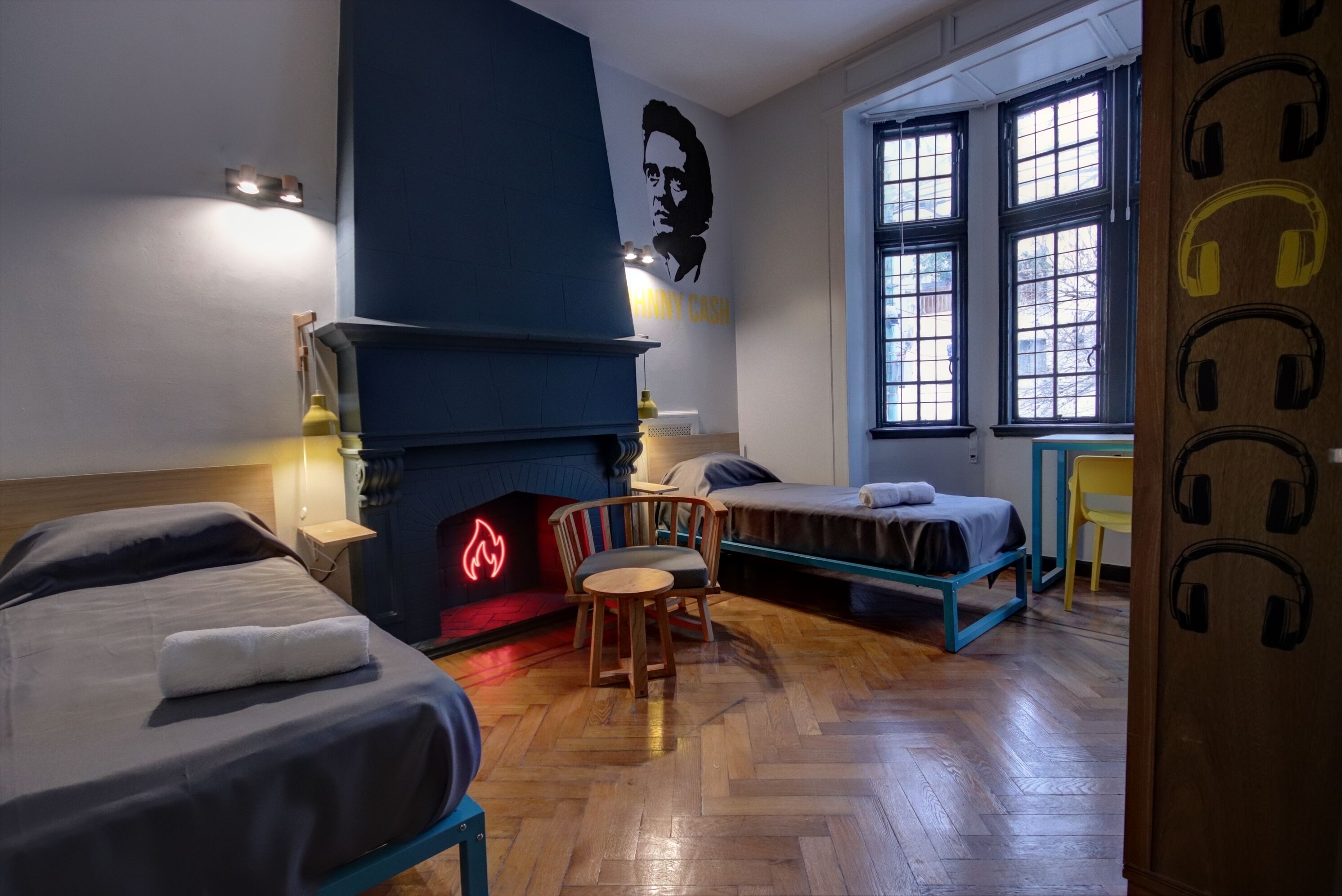 A room with two beds, a fireplace, a wall mural, and large windows.