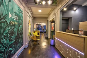 A hotel reception area with a mural, a reception desk, a seating area, and a hallway leading to a room. - Play Hostel Garden (Buenos Aires)