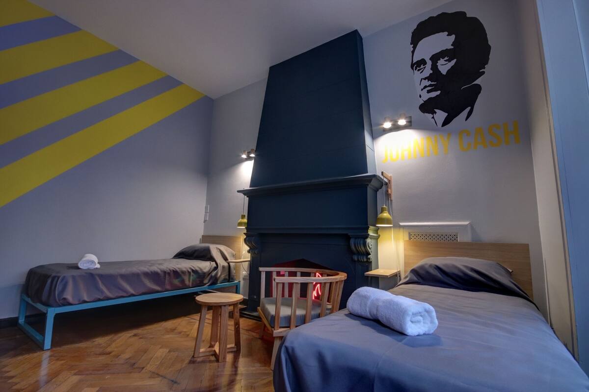 Hotellihuone, jossa on kaksi erillistä sänkyä, takka ja seinämaalaus.