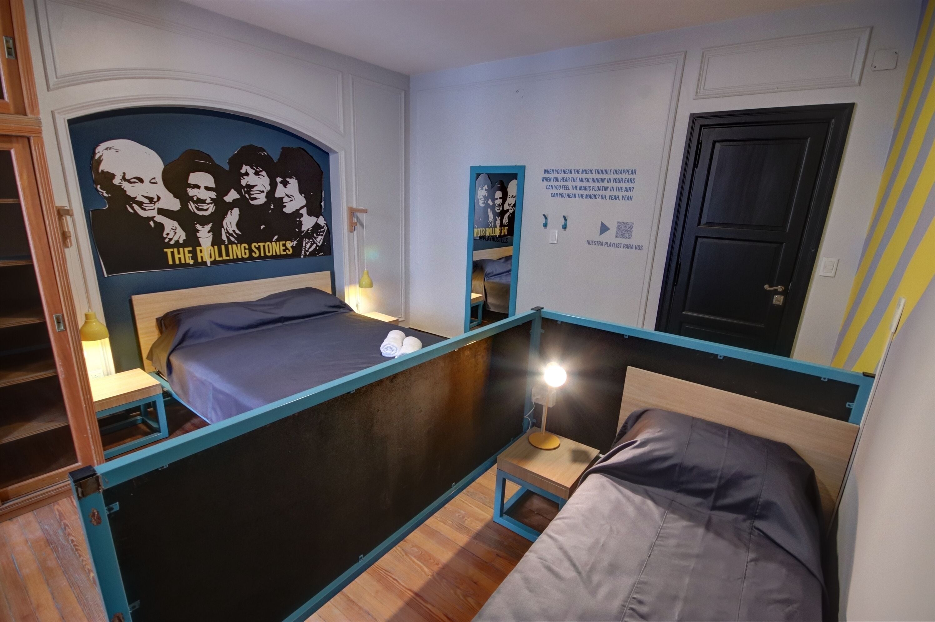Un dormitorio con una litera, un cartel de The Rolling Stones, un cartel con texto relacionado con la música y una puerta con cerradura.