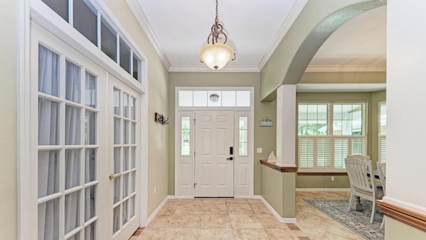 A hallway with a white door, a chandelier, and a dining area with a table and chairs. - Garden House with Pool & Spa (Bradenton)