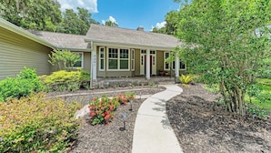 A single-story house with a covered porch, a front yard with mulch and plants, and a clear sky. - Garden House with Pool & Spa (Bradenton)