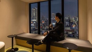 A man sitting on a bench by a large window with a cityscape view.
