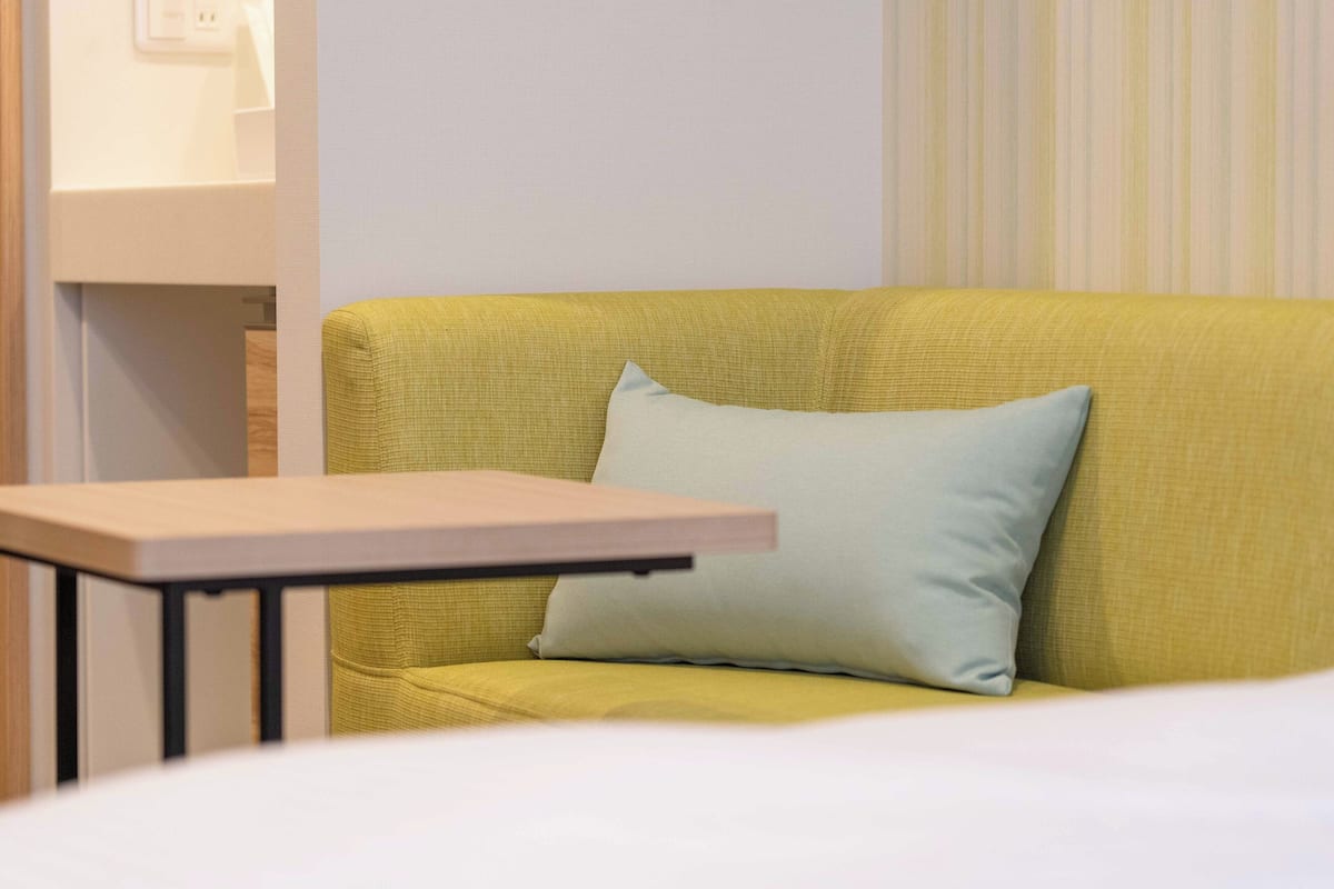 A yellow sofa with a light blue pillow, a small wooden table, and a white wall with a striped pattern.