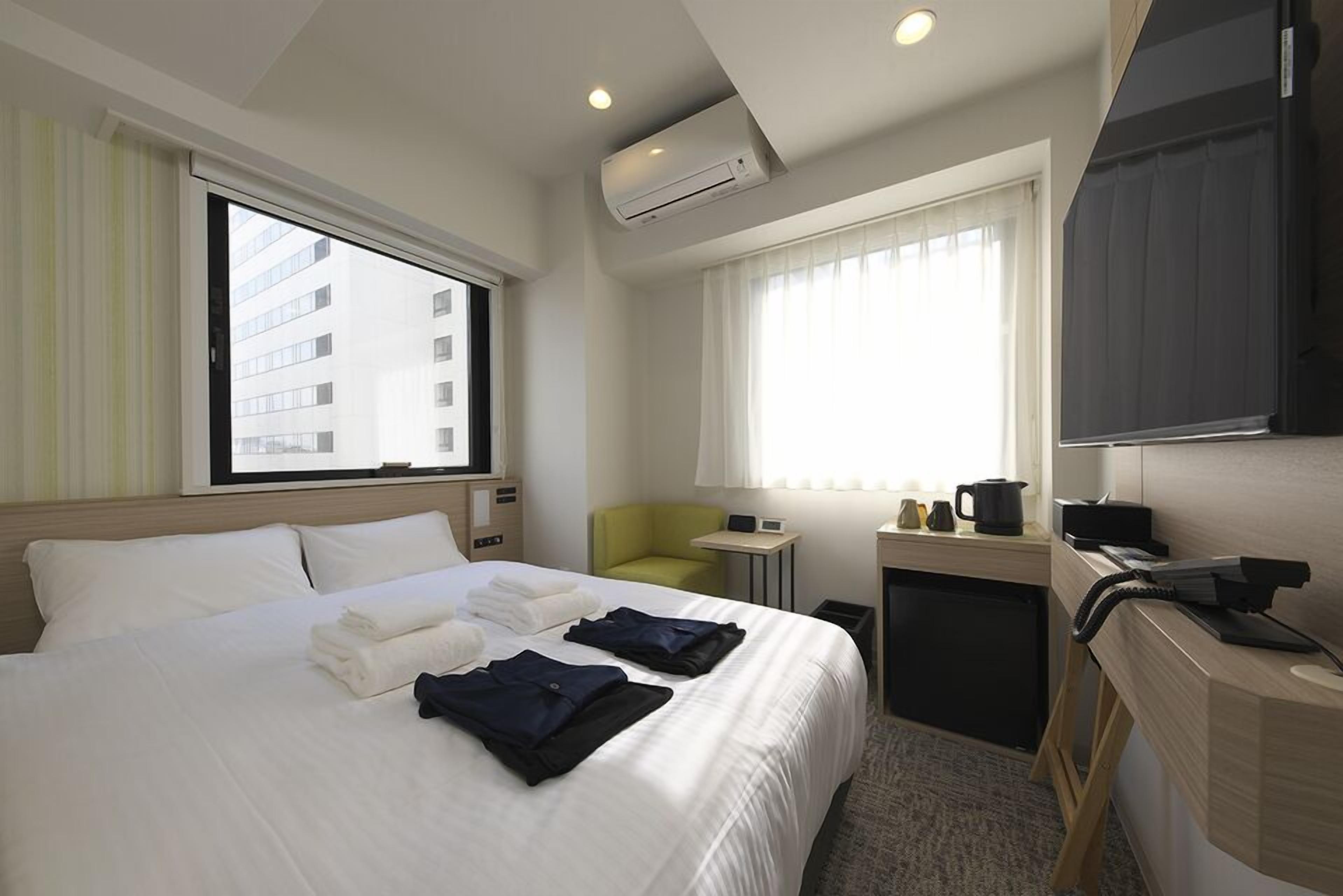 Hotelkamer met een bed, een bureau, een stoel, een airconditioner en een raam met gordijnen.
