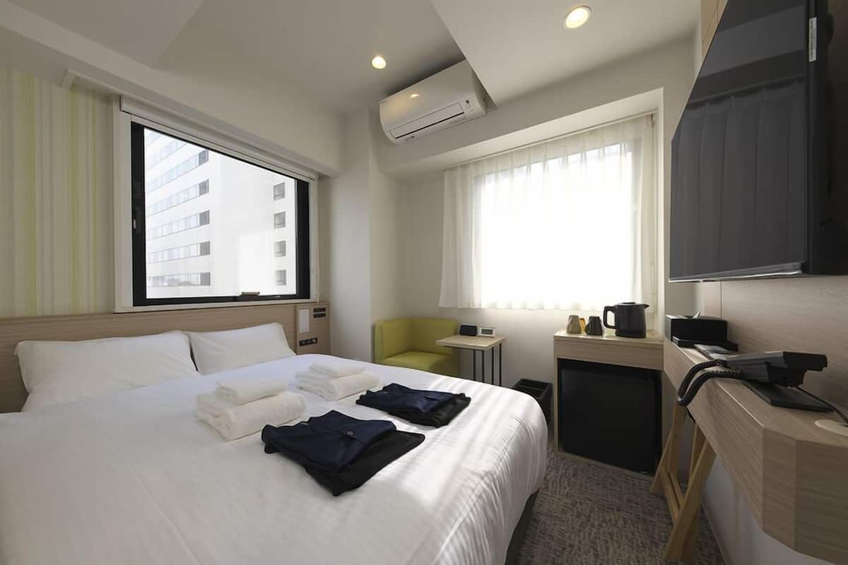 A hotel room with a bed, a desk, a chair, an air conditioning unit, and a window with curtains.
