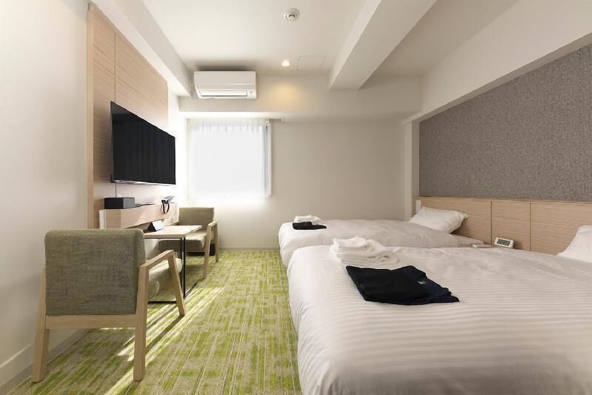 A hotel room with two beds, a desk with a chair, a television, and a window with curtains.