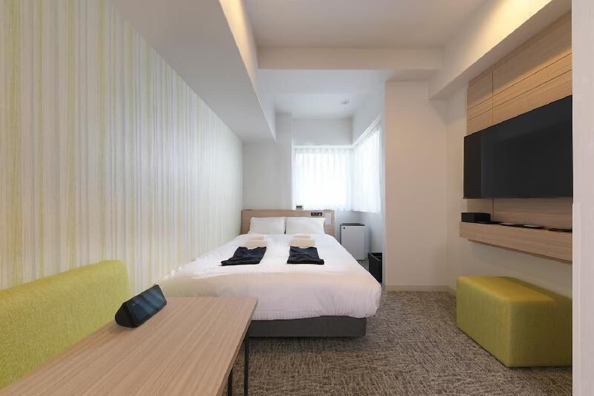 A hotel room with a bed, a desk, a chair, a TV, and a window.