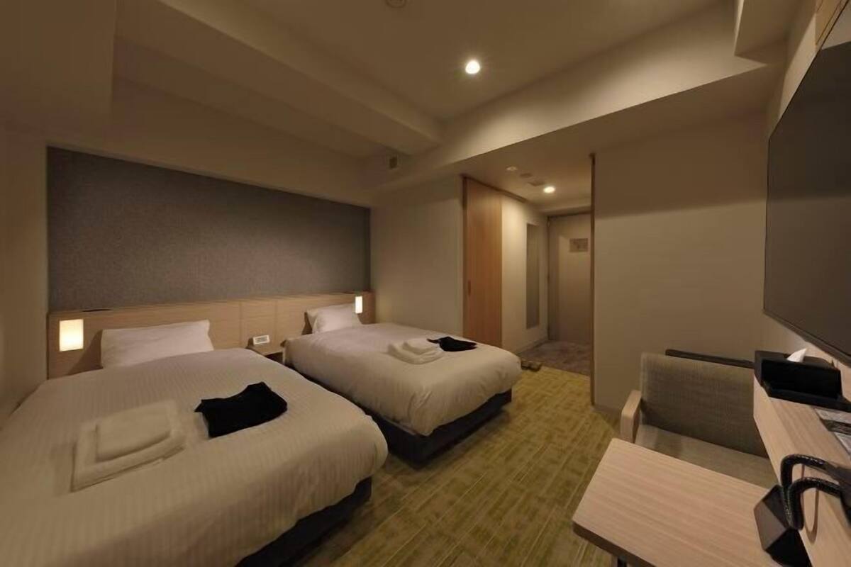A hotel room with two beds, a desk, a chair, a television, and a door leading to another room.