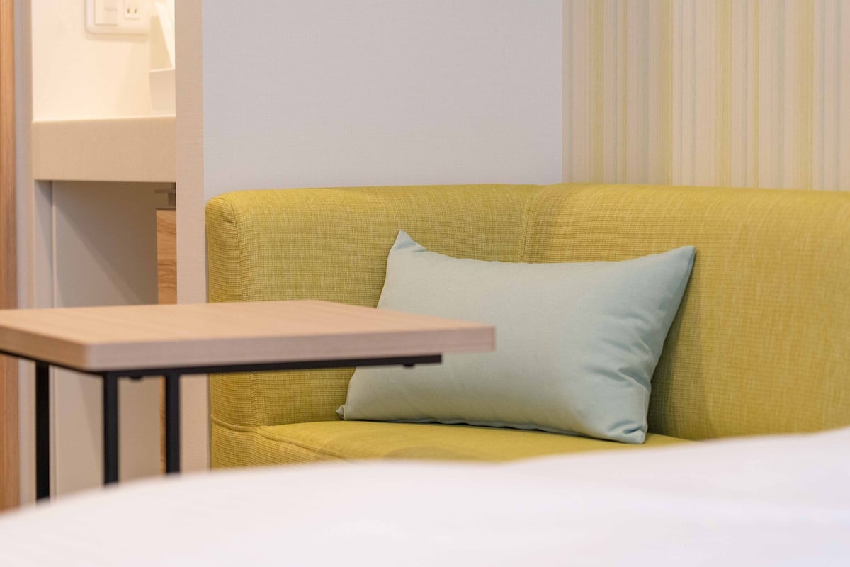 A yellow sofa with a light blue pillow, a small wooden table, and a white wall with a striped pattern.
