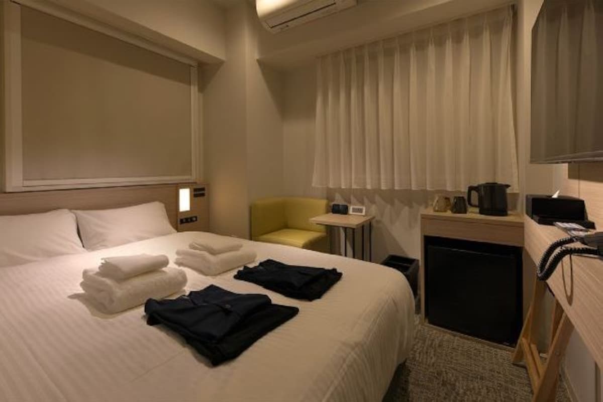 Habitación de hotel con cama, escritorio, silla, mesita y ventana con cortinas.