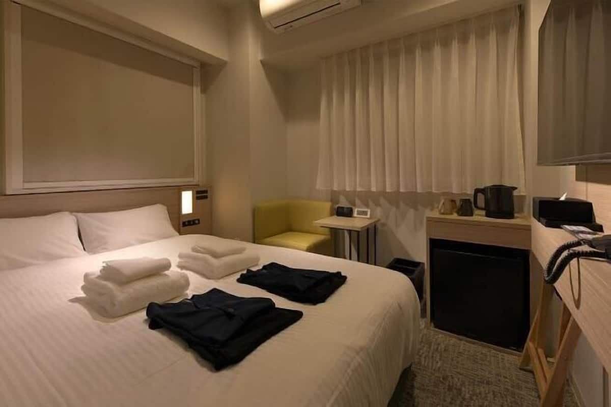A hotel room with a bed, a desk, a chair, a small table, and a window with curtains.