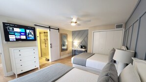 A modern bedroom with a TV displaying streaming services, a ceiling fan, a walk-in closet, and a desk with a lamp.