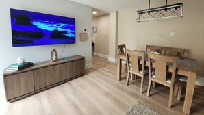 A modern living room with a flat-screen TV, wooden furniture, and a dining area.