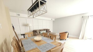 A modern living room with a dining area, featuring a wooden table, chairs, a sofa, and a unique geometric pendant light.