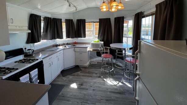 Una cocina compacta con gabinetes blancos, estufa, microondas y una zona de comedor con dos taburetes de bar.